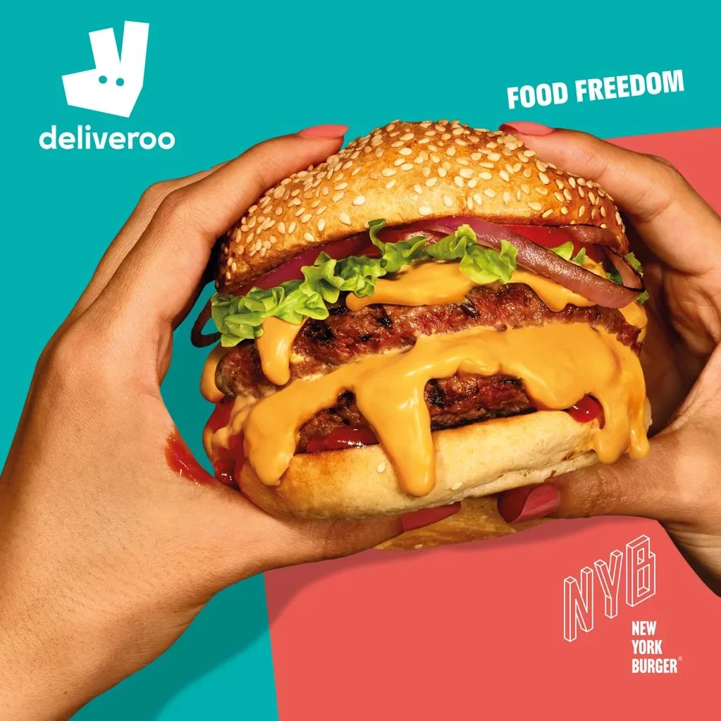 A person holding a cheeseburger with lettuce, tomato, cheese, and bacon against a colorful background with the logos of Deliveroo and New York Burger, and the text "Food Freedom".