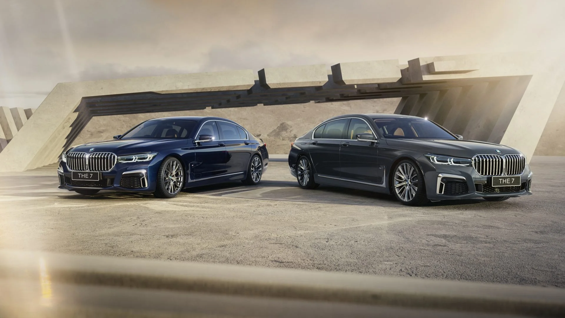Two luxury BMW sedans parked outdoors under modern architectural structure, with a desert landscape in the background.