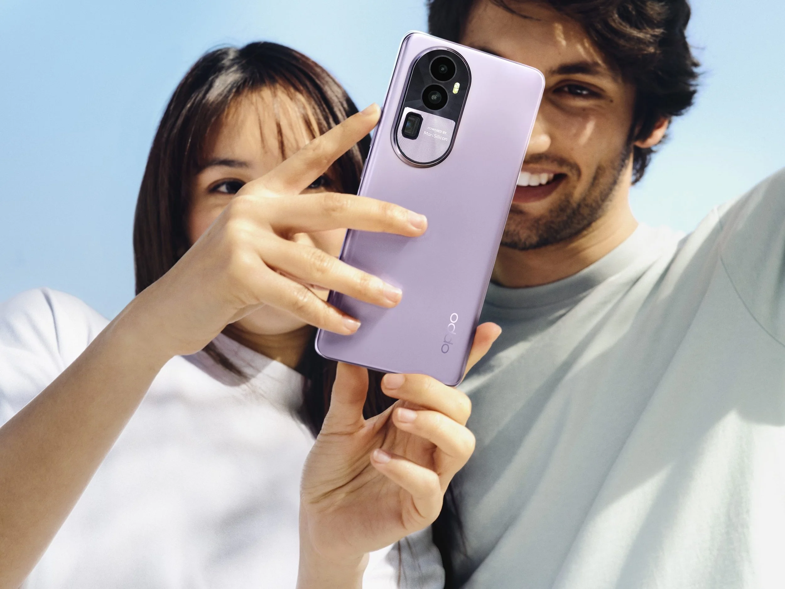 A woman and a man taking a selfie with a smartphone against a light blue background. The woman is holding the phone, and the man is smiling.