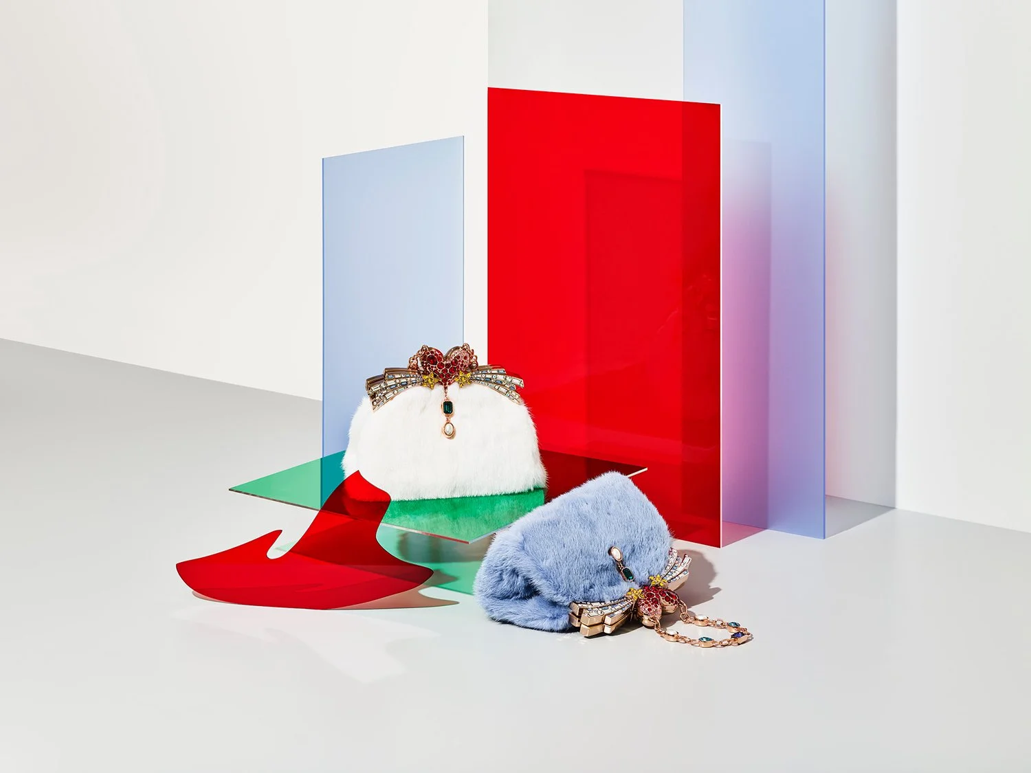 Two colorful handbags with jewelry embellishments sit on a white surface, with geometric colored panels in the background.