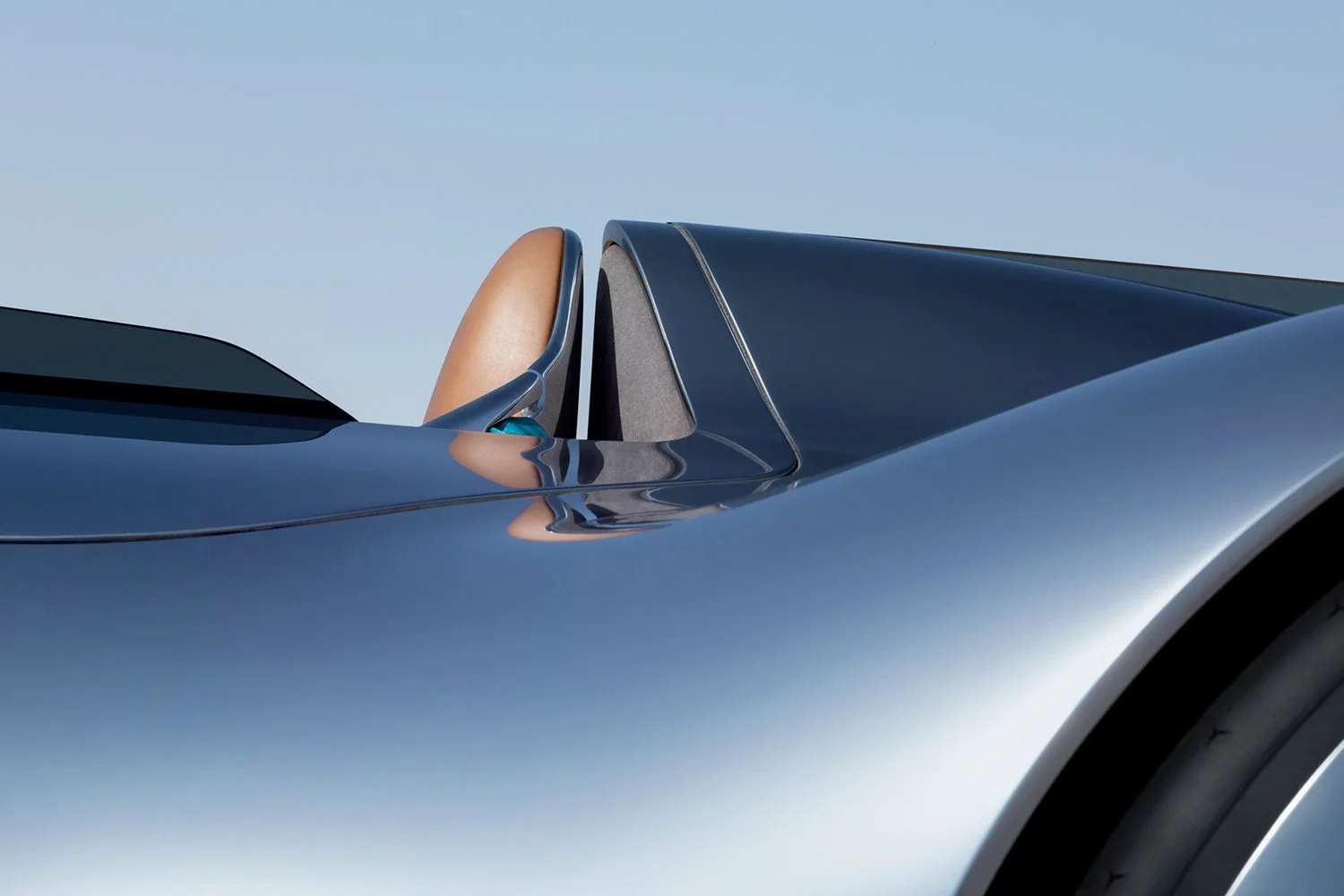 Close-up of a sleek blue convertible sports car with the driver's seat visible and a clear sky in the background.