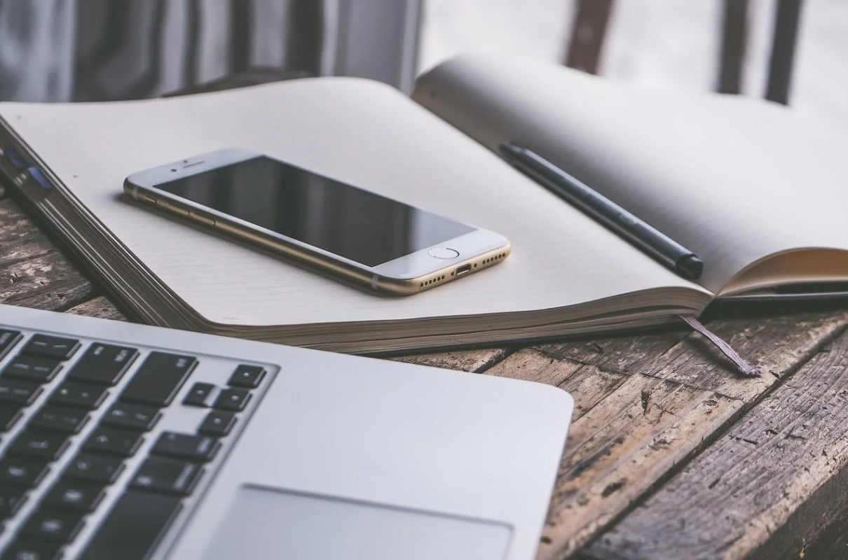 Offene Notizbuch mit Stift, Smartphone, Laptop, auf Holztisch an Fenster