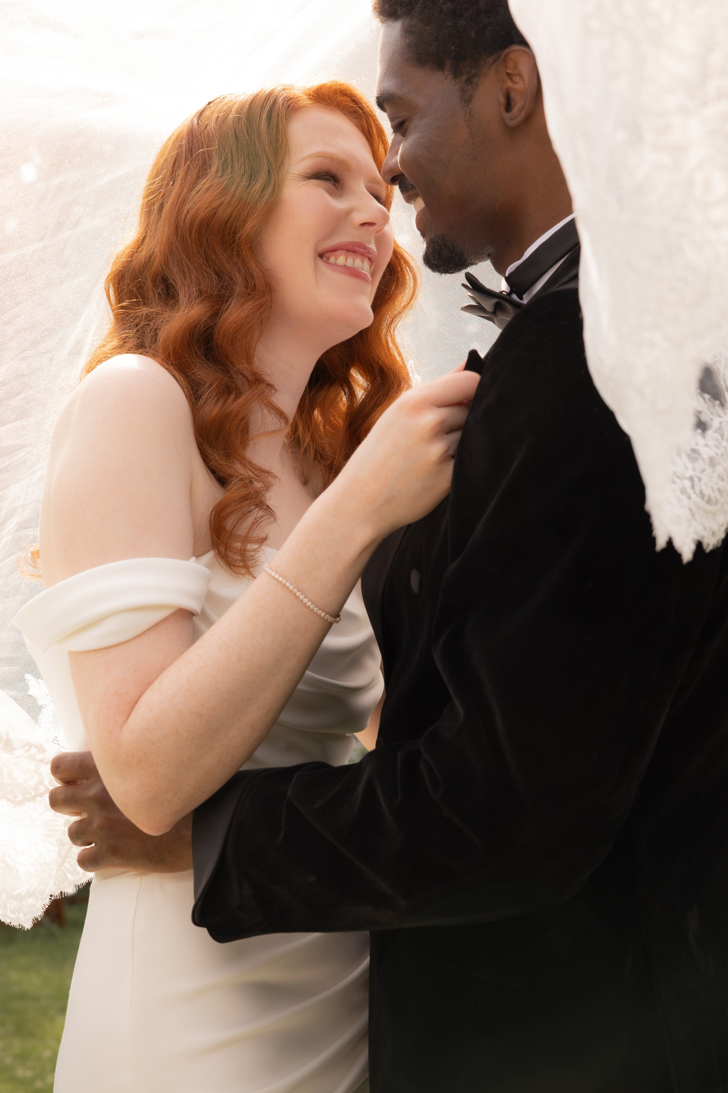 A couple in wedding attire smiling and looking into each other's eyes, close-up, outdoor setting.