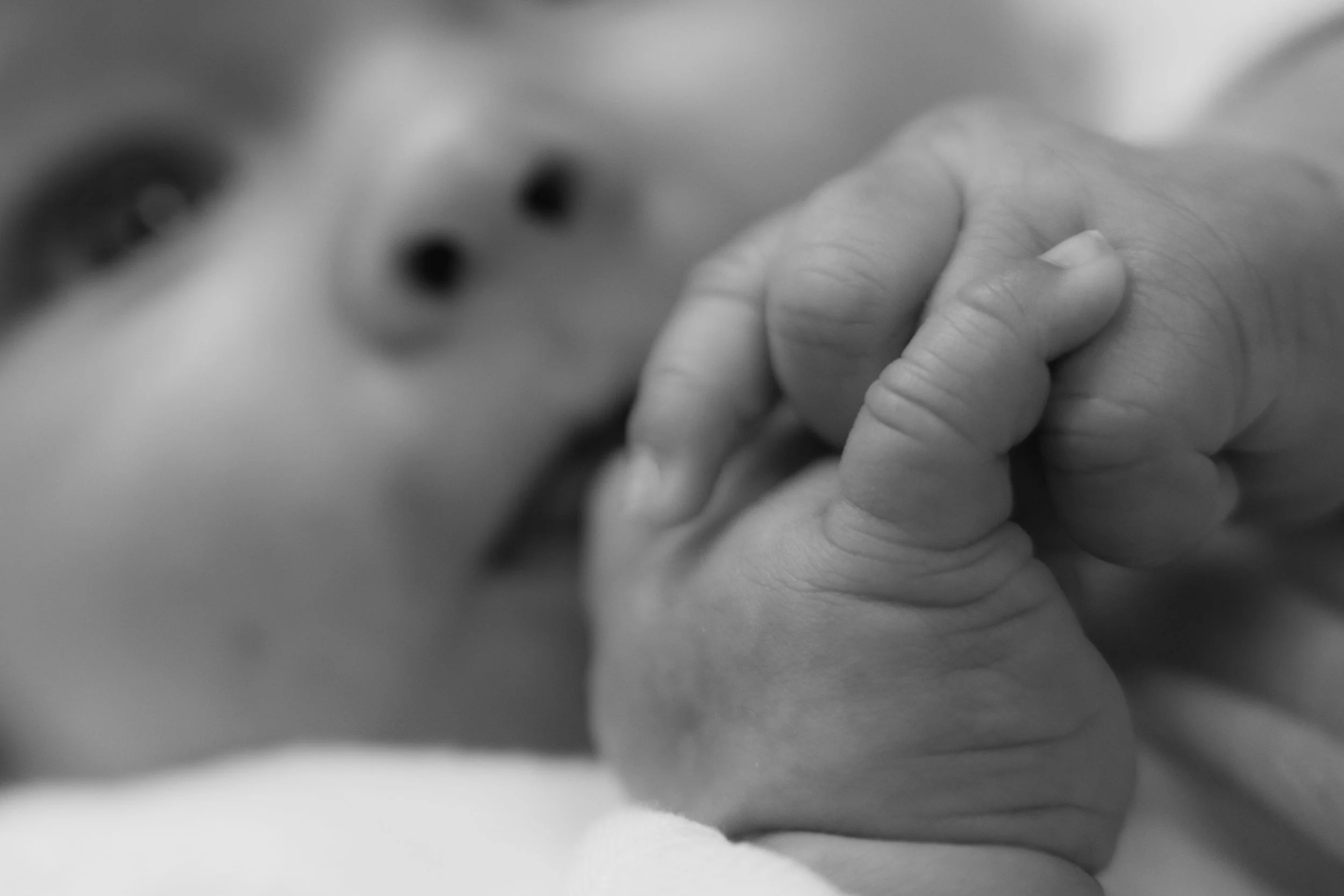 Close-up of a baby's face and hand, black and white photo.
