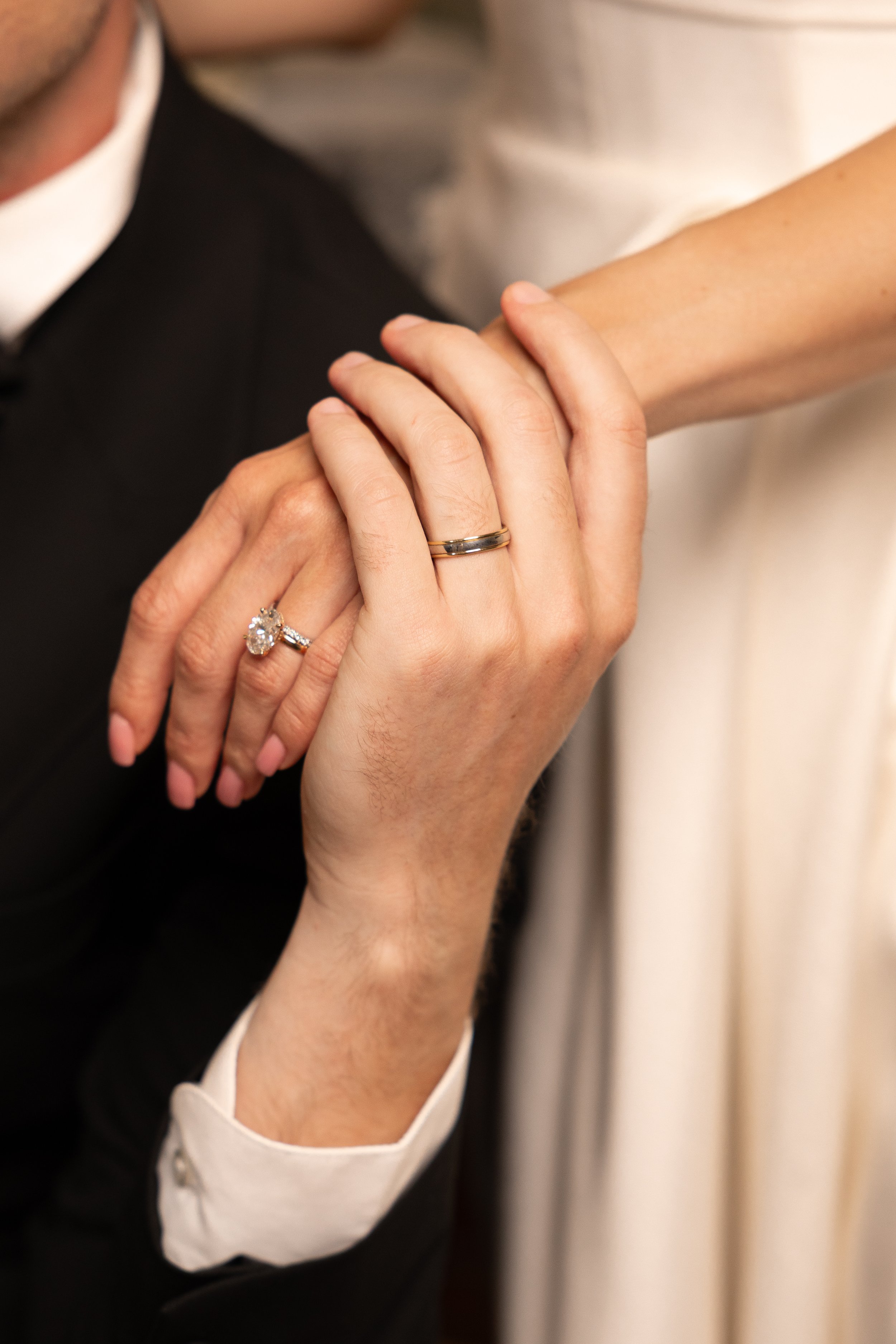 Close-up of a woman and a man holding hands; both are wearing wedding rings, with the focus on their intertwined hands.