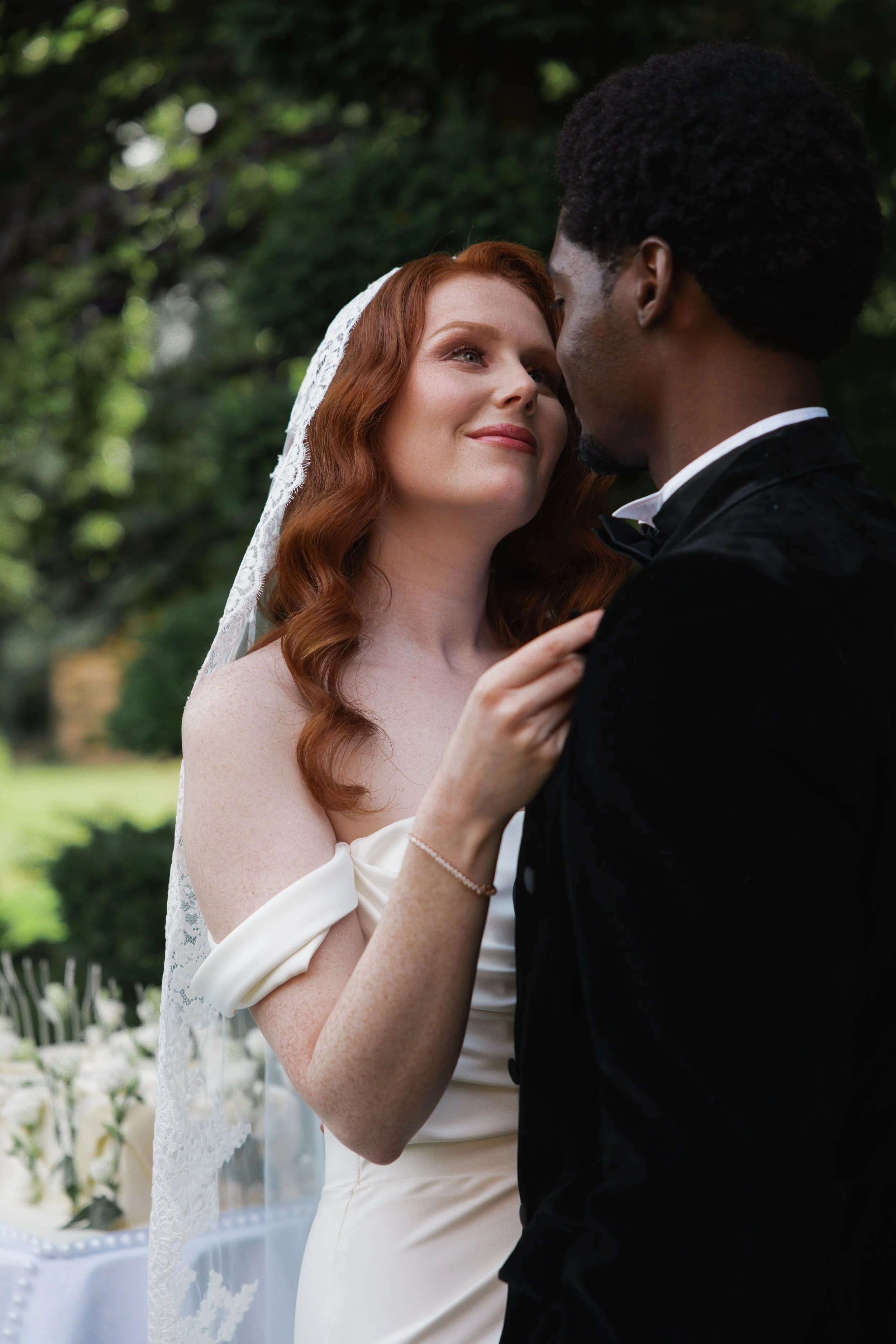 A bride and groom share a close moment outdoors, gazing into each other's eyes during a wedding ceremony surrounded by greenery.