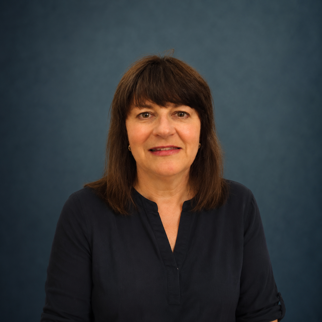 A middle-aged woman with shoulder-length brown hair smiling in front of a dark blue backdrop.