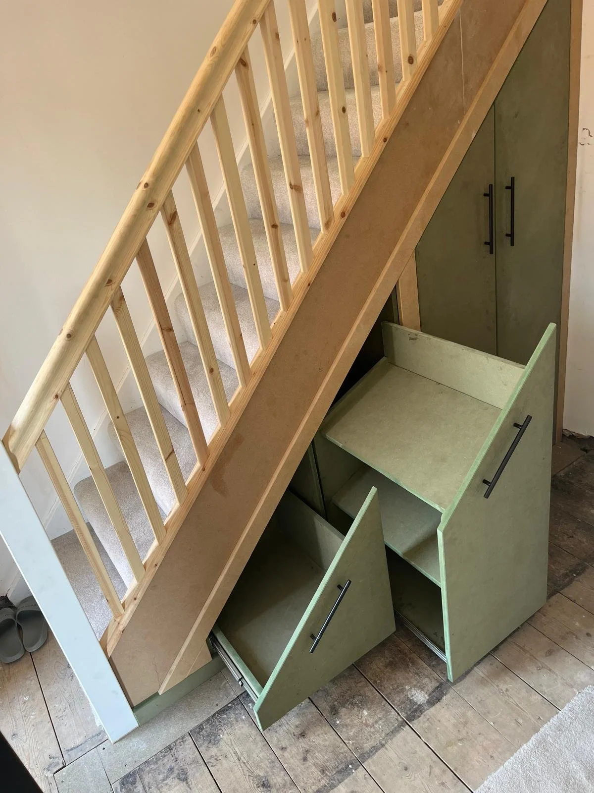 A staircase with a wooden handrail and gray carpeted steps, with built-in green cabinets underneath, some doors open, showing storage space.
