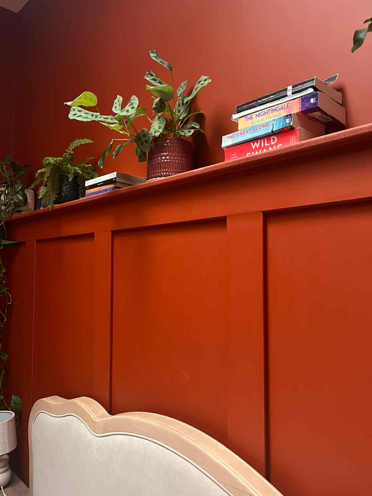 Red wooden headboard with a shelf on top, decorated with potted plants and stacked books.