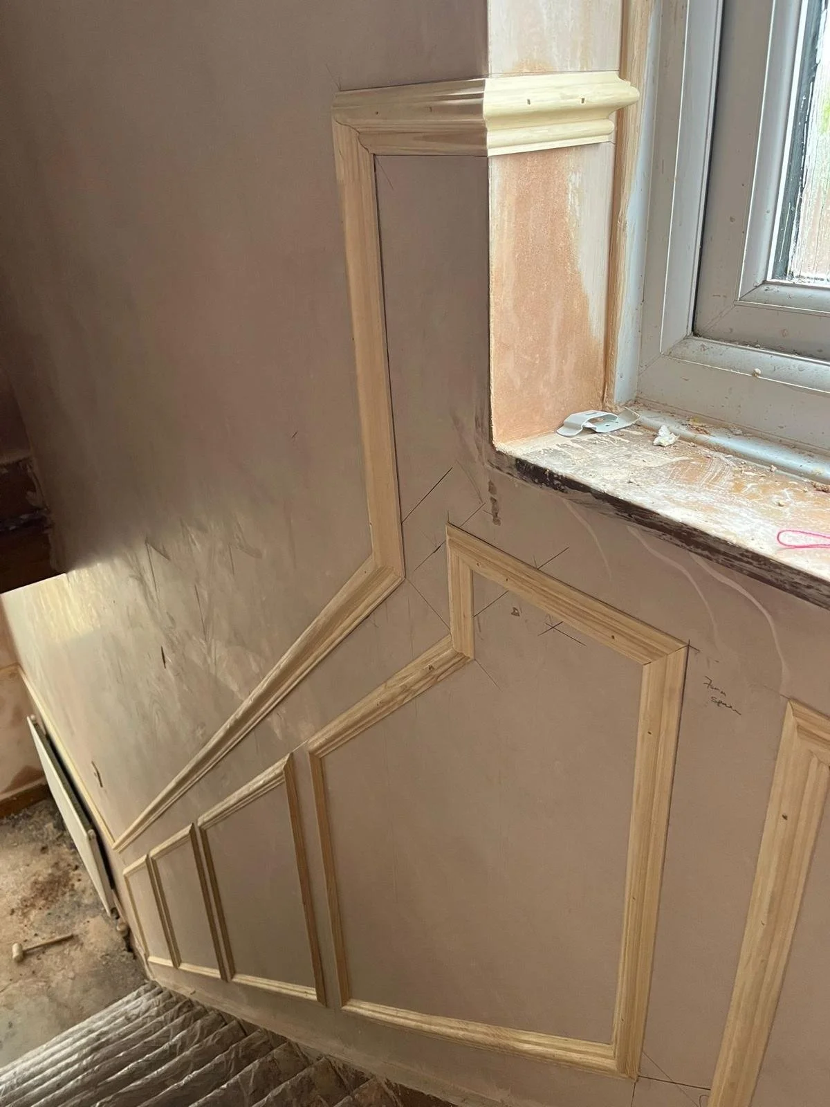 Wooden framing and molding are being installed around a window in a room under renovation.
