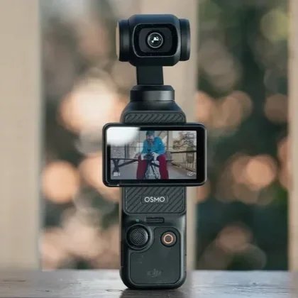 A handheld camera stabilizer with a mounted camera and a small screen showing a person sitting outdoors.