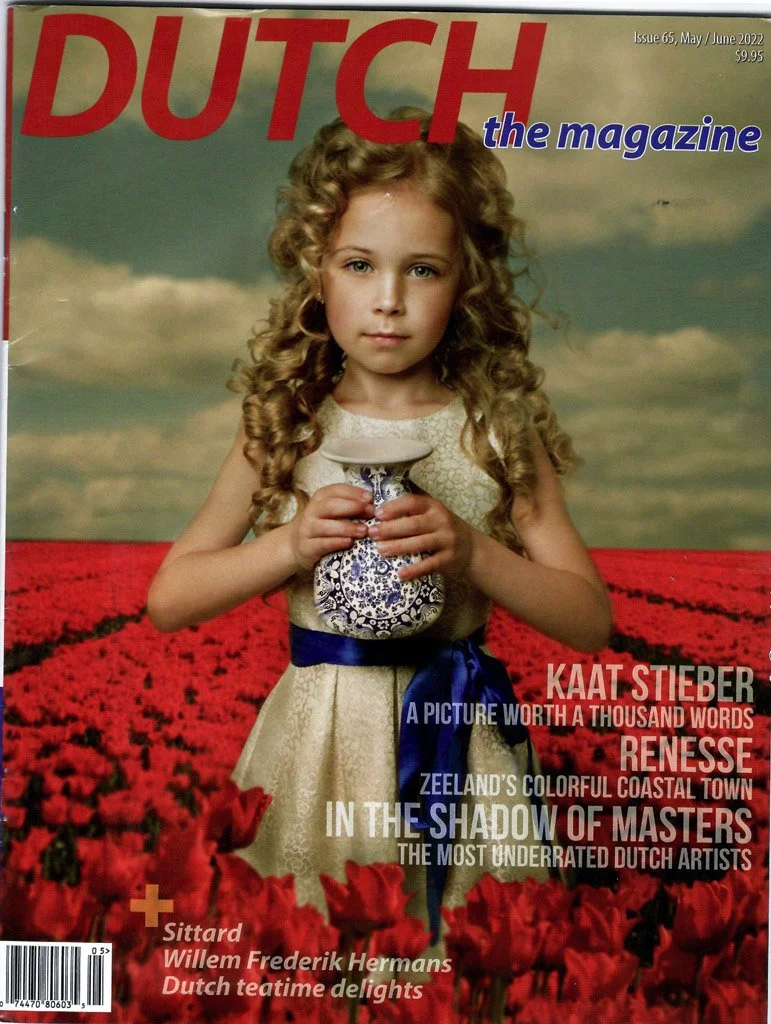 De cover van een magazine genaamd 'DUTCH, the magazine', met een jonge meisje met krullend haar die in een veld met rood bloemen staat, met een wolkige hemel op de achtergrond.