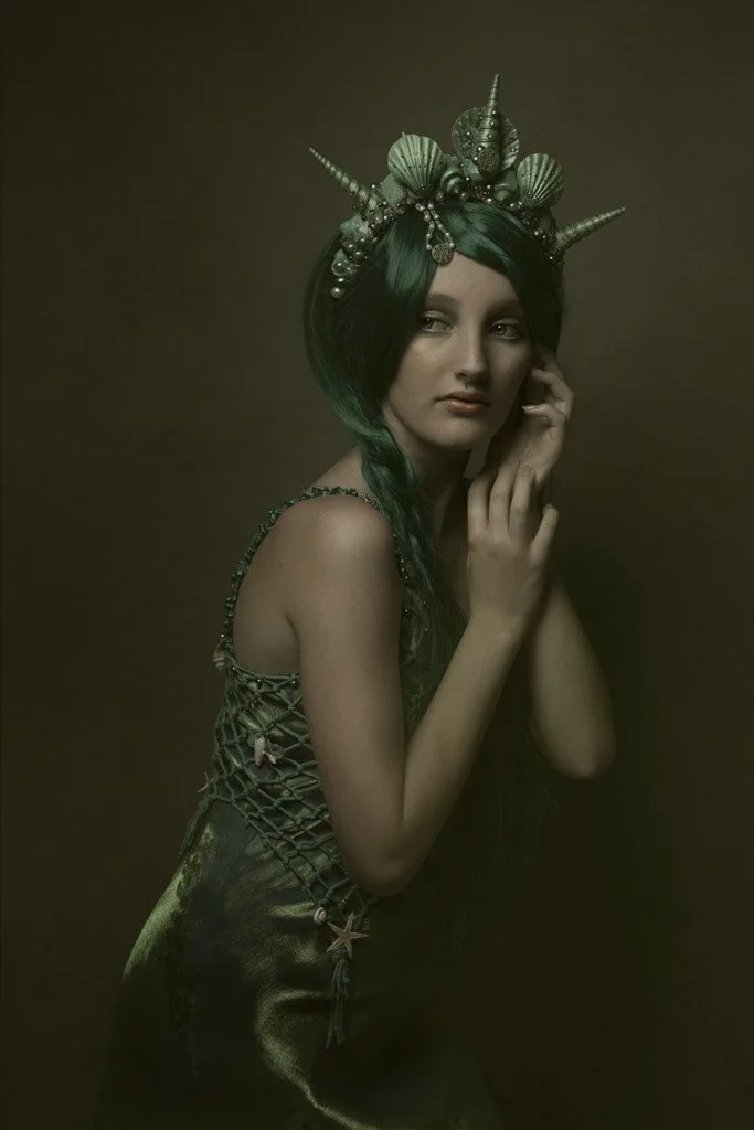 Vrouw met lange groene haar, donker gewaad en een sierlijke hoofdband met zeeachtige en zeester- en zeeschelp-achtige details.