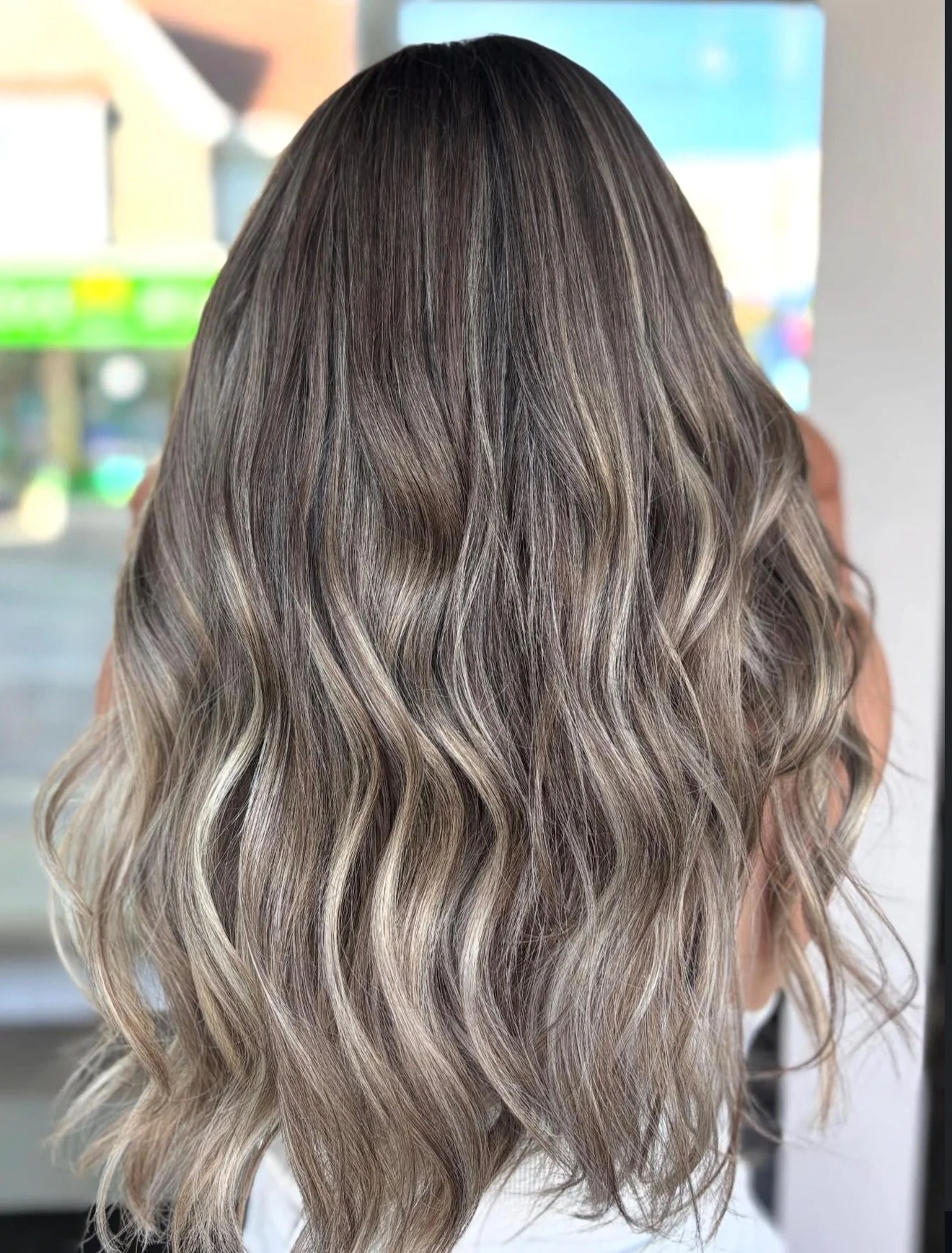 Back of a woman with long, wavy hair featuring a blend of dark and blonde highlights.