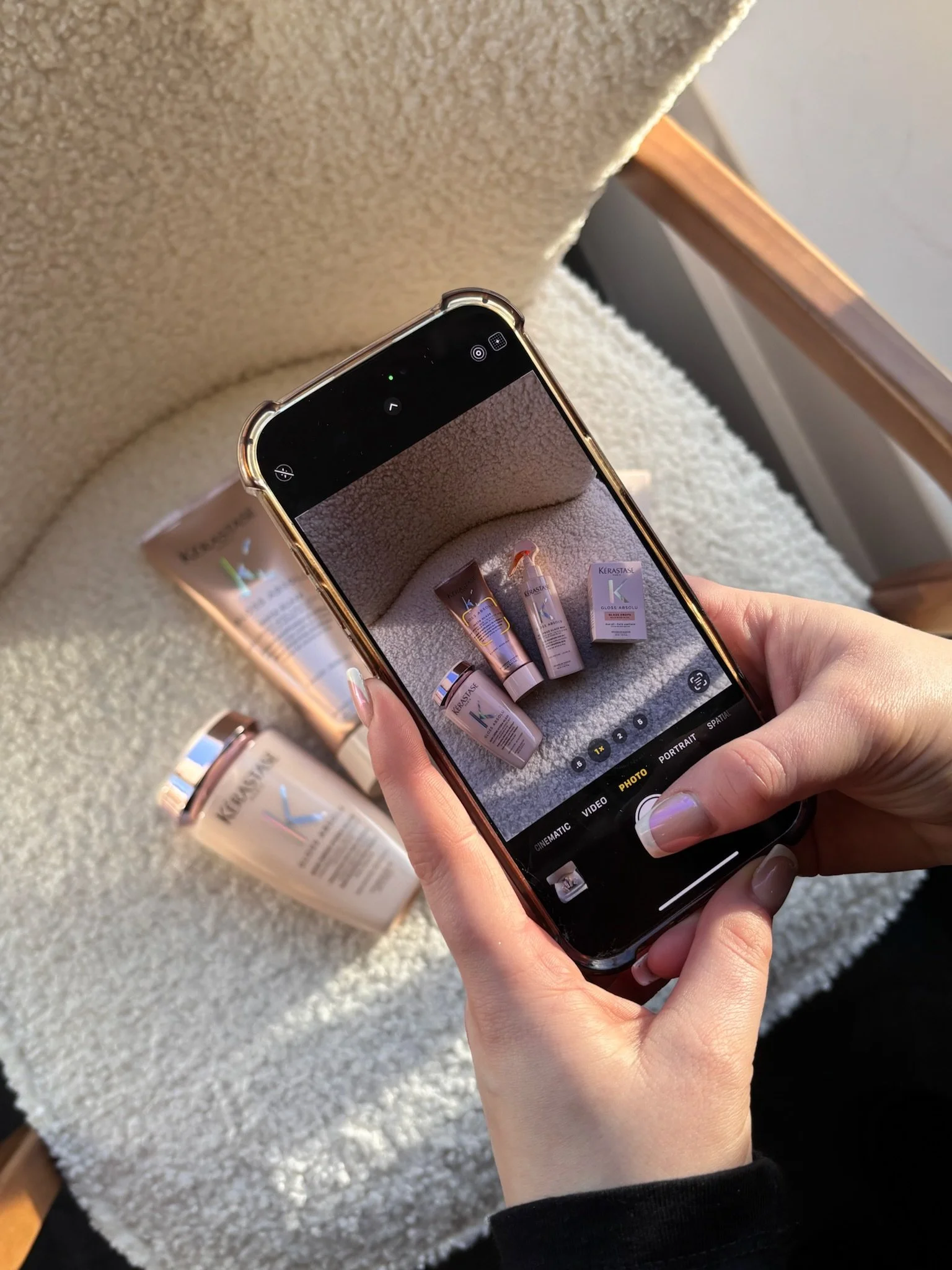 A person is taking a photo of skincare products with a phone, positioned over a soft, light-colored fabric surface.