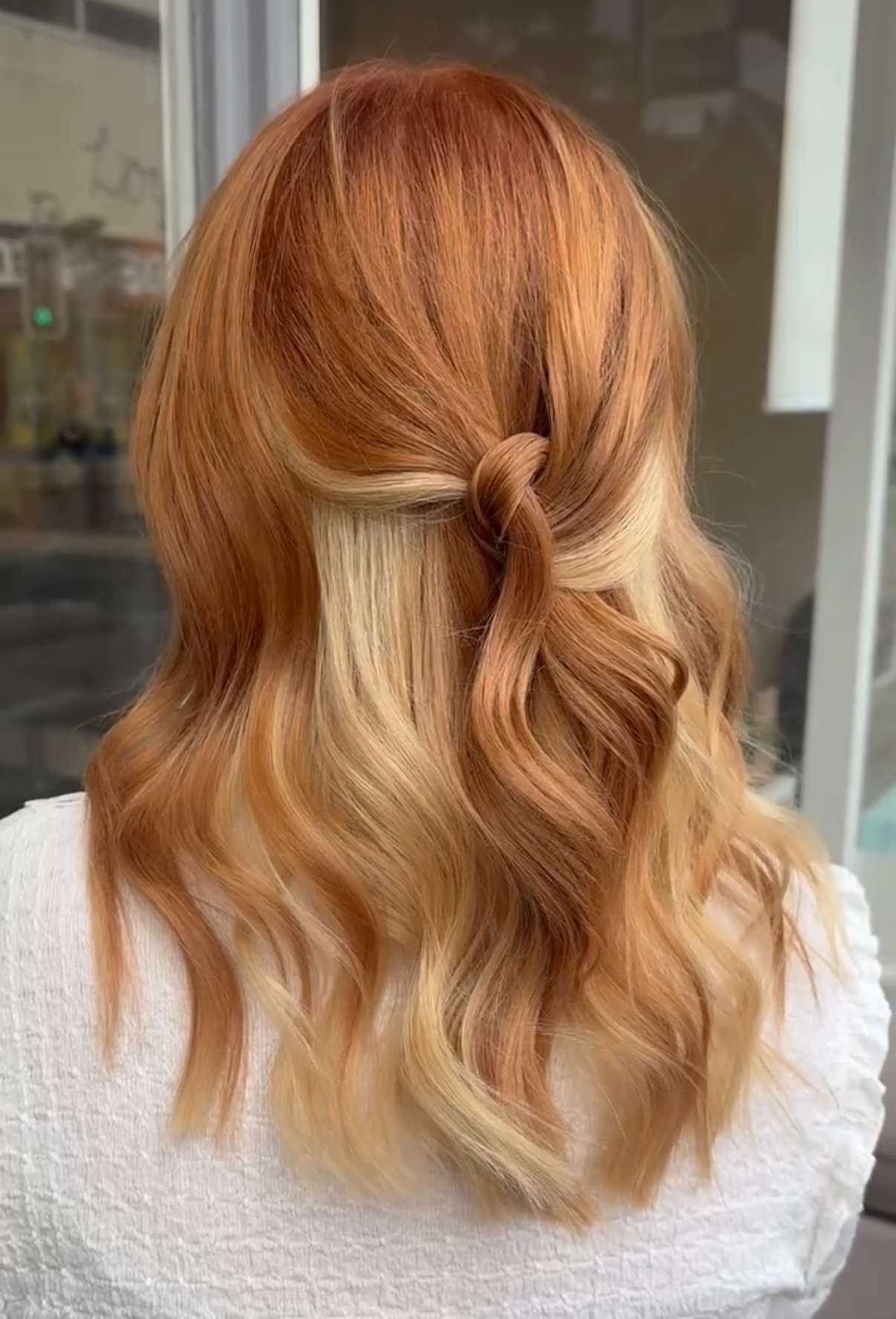 Back view of a woman with long, wavy, red hair styled with a twist knot at the back.