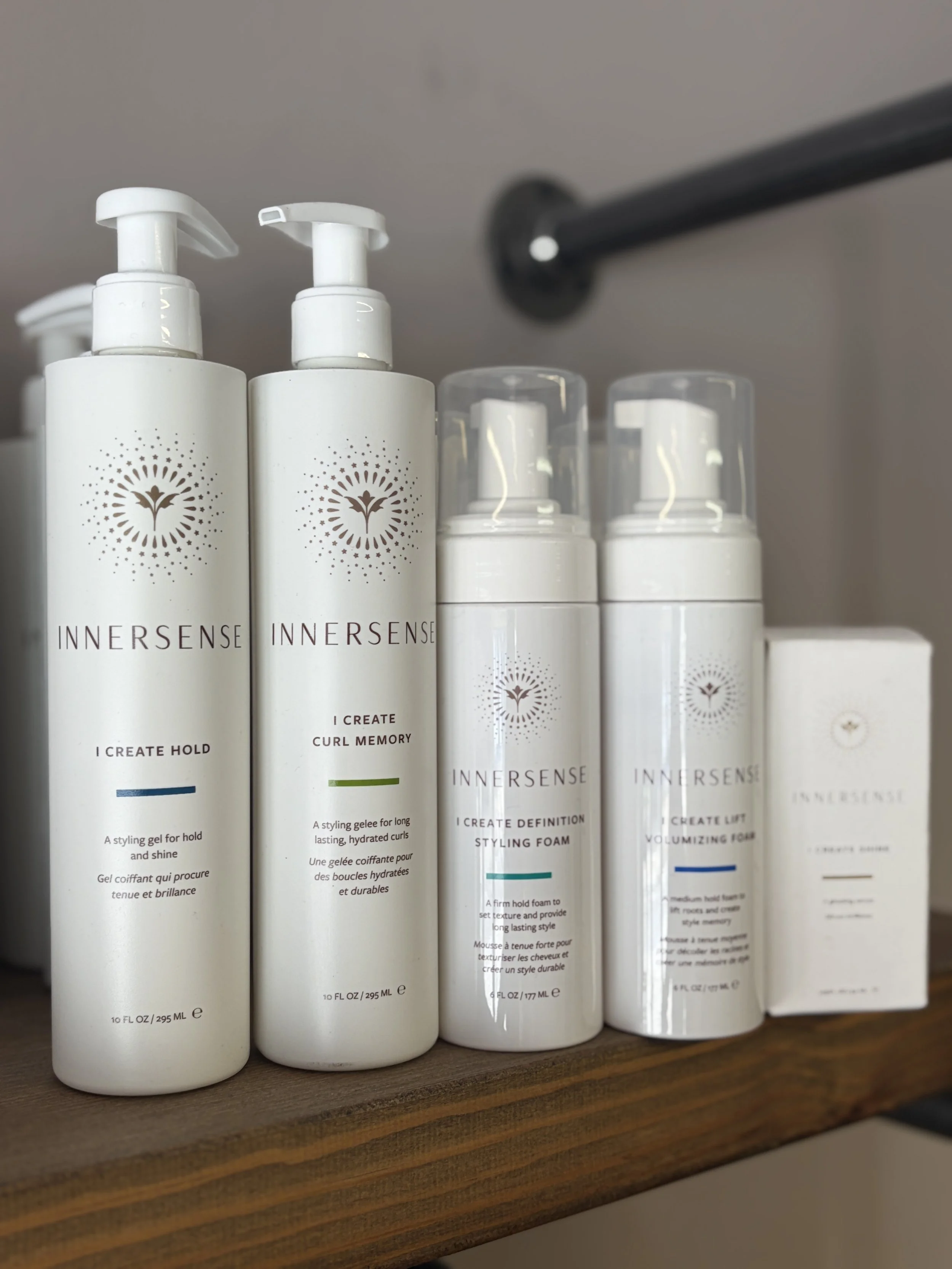 Close-up of several white bottles of hair styling products with pump dispensers and transparent caps, labeled 'INNERSENSE' on a wooden shelf.