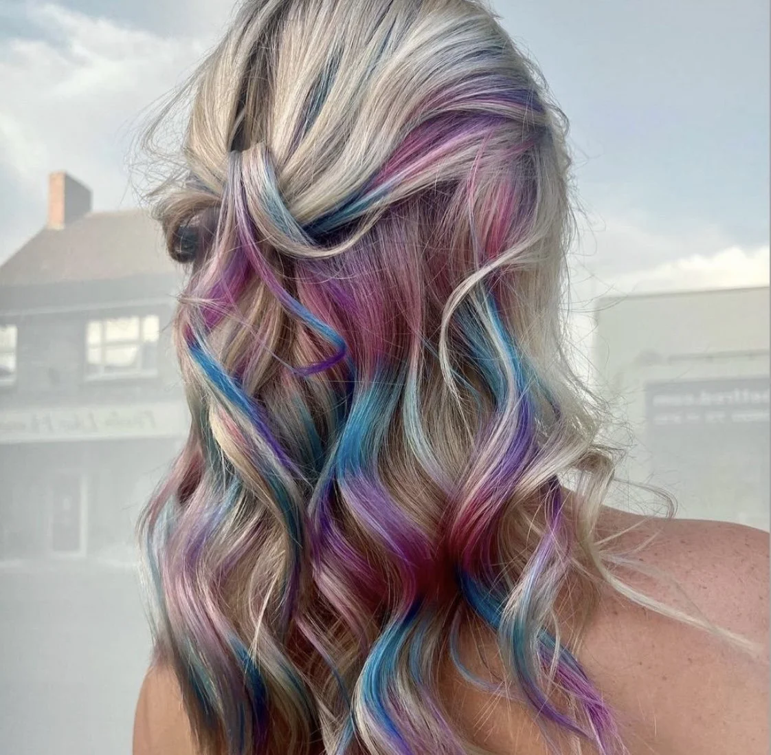 A woman with long, wavy blonde hair with streaks of purple, pink, blue, and teal.