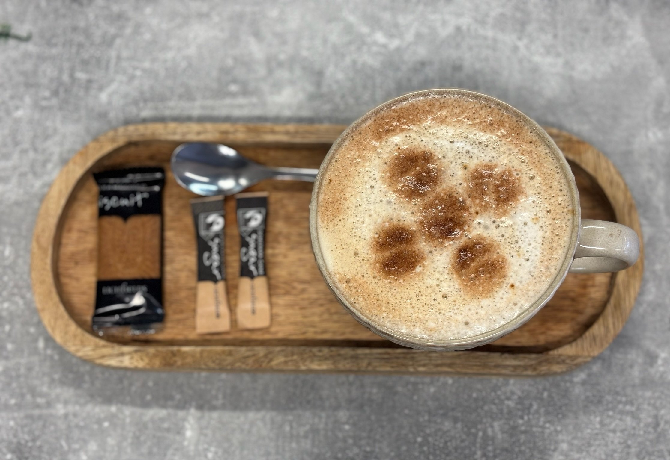 A top view of a glass of frothy cappuccino with cinnamon or cocoa powder sprinkled on top, placed on a wooden tray.