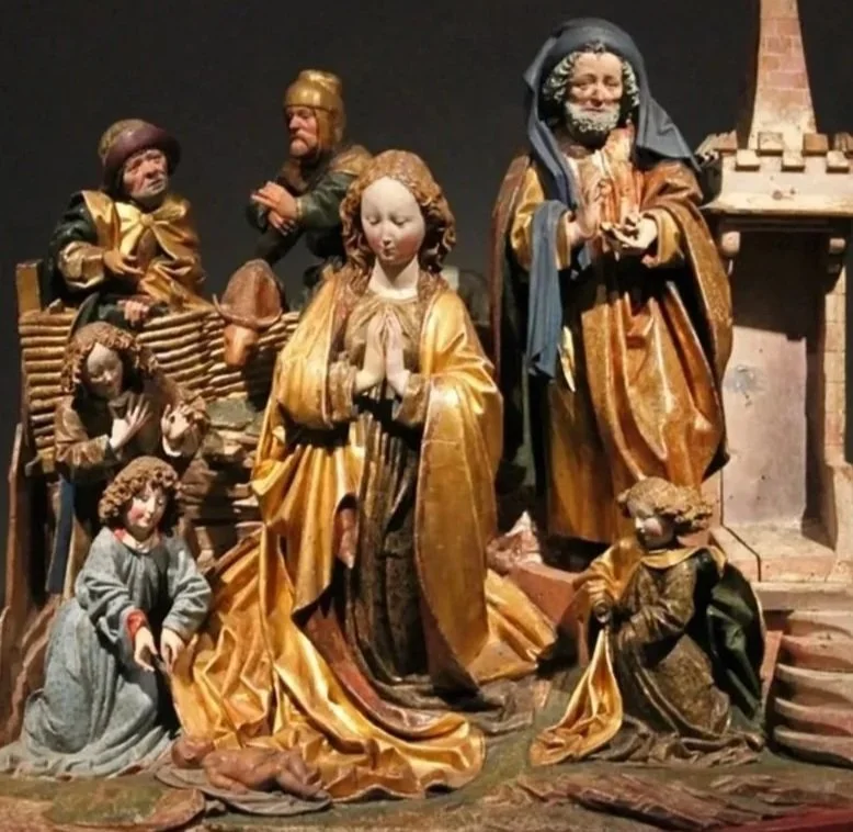 Beeld van houtsculpturen van de Heilige Familie met kinderen, met goudkleurige kleding, in een gangbare kerststalletjes-sfeer.