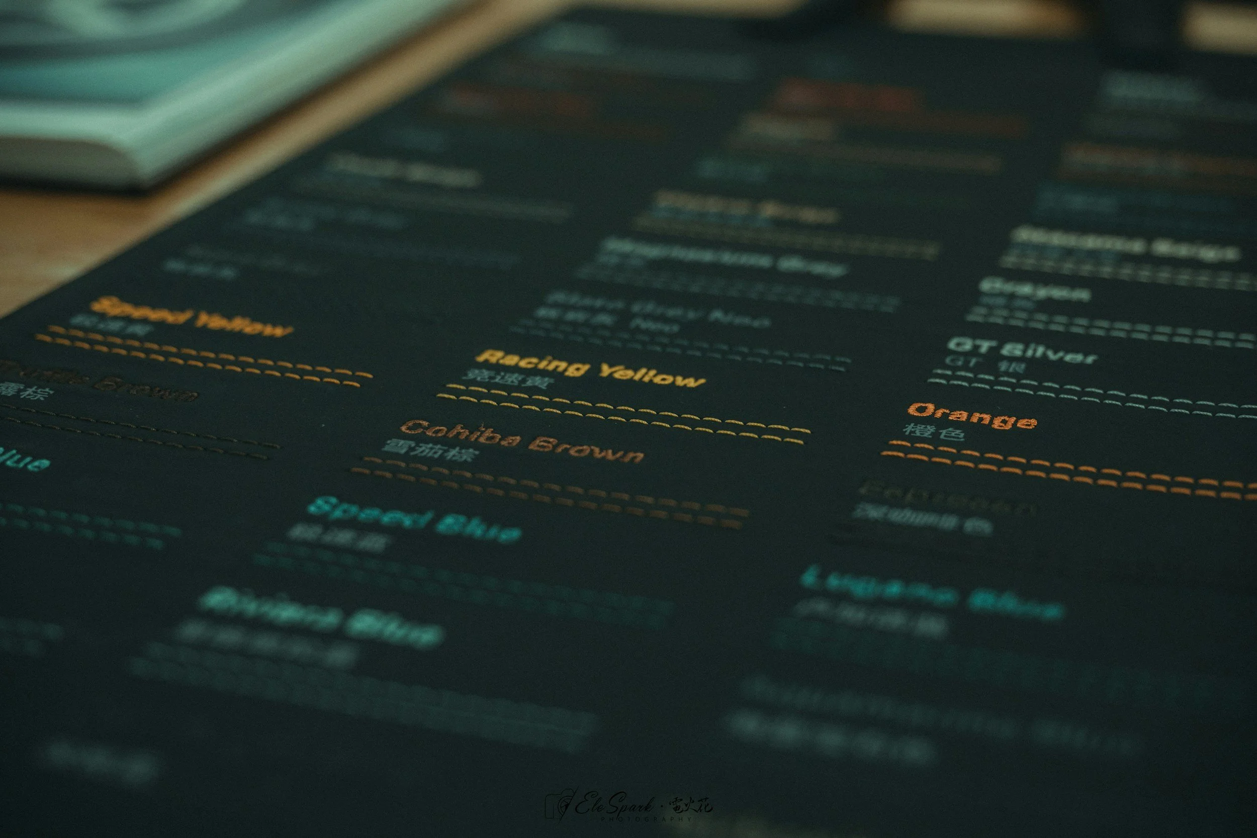 Close-up of a dark sheet with colorful printed text and lines, possibly a menu or chart, with parts of a laptop and other objects in the background.