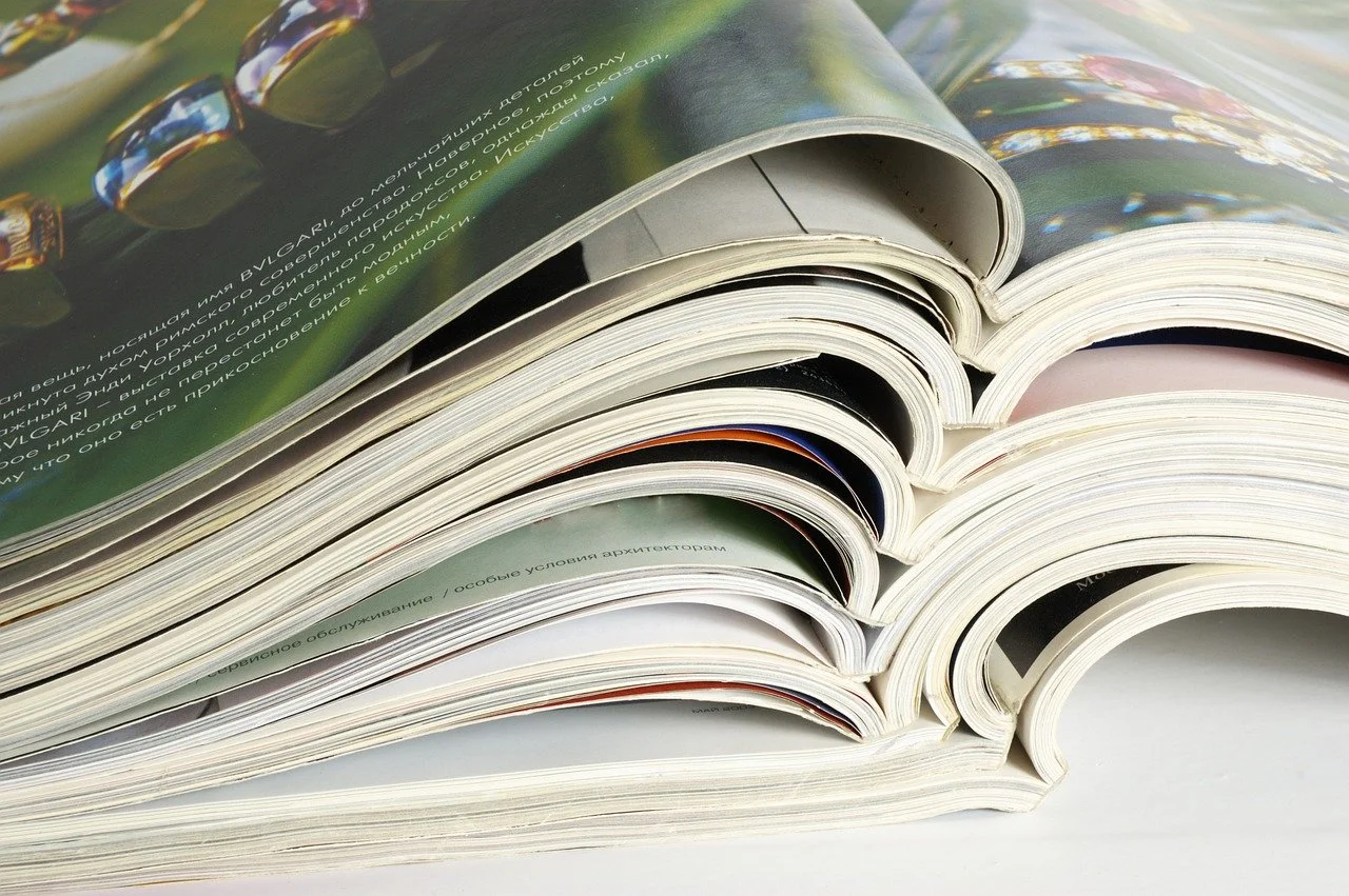 A close-up view of stacked magazines with pages slightly curled, showing colorful images and text in Russian.