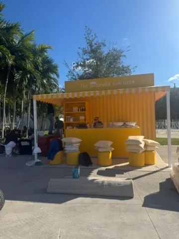 Yellow and orange outdoor sunshade stand with towels and soap on display, with palm trees and a bright blue sky in the background.