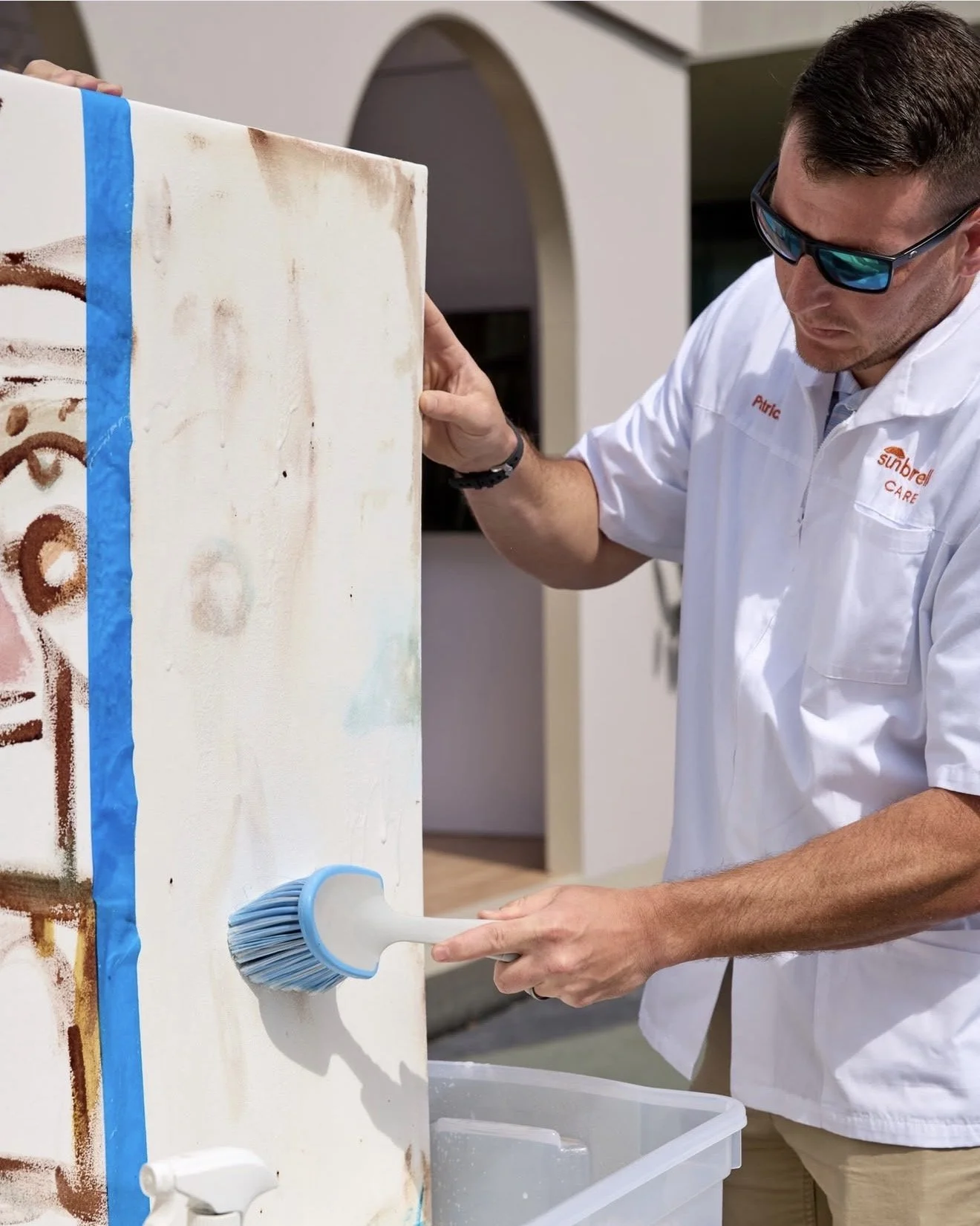 A man cleaning a white painted surface with a large scrubbing brush.