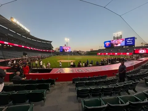 Empty baseball stadium with a cleared field and few people sitting in the stands during sunset.