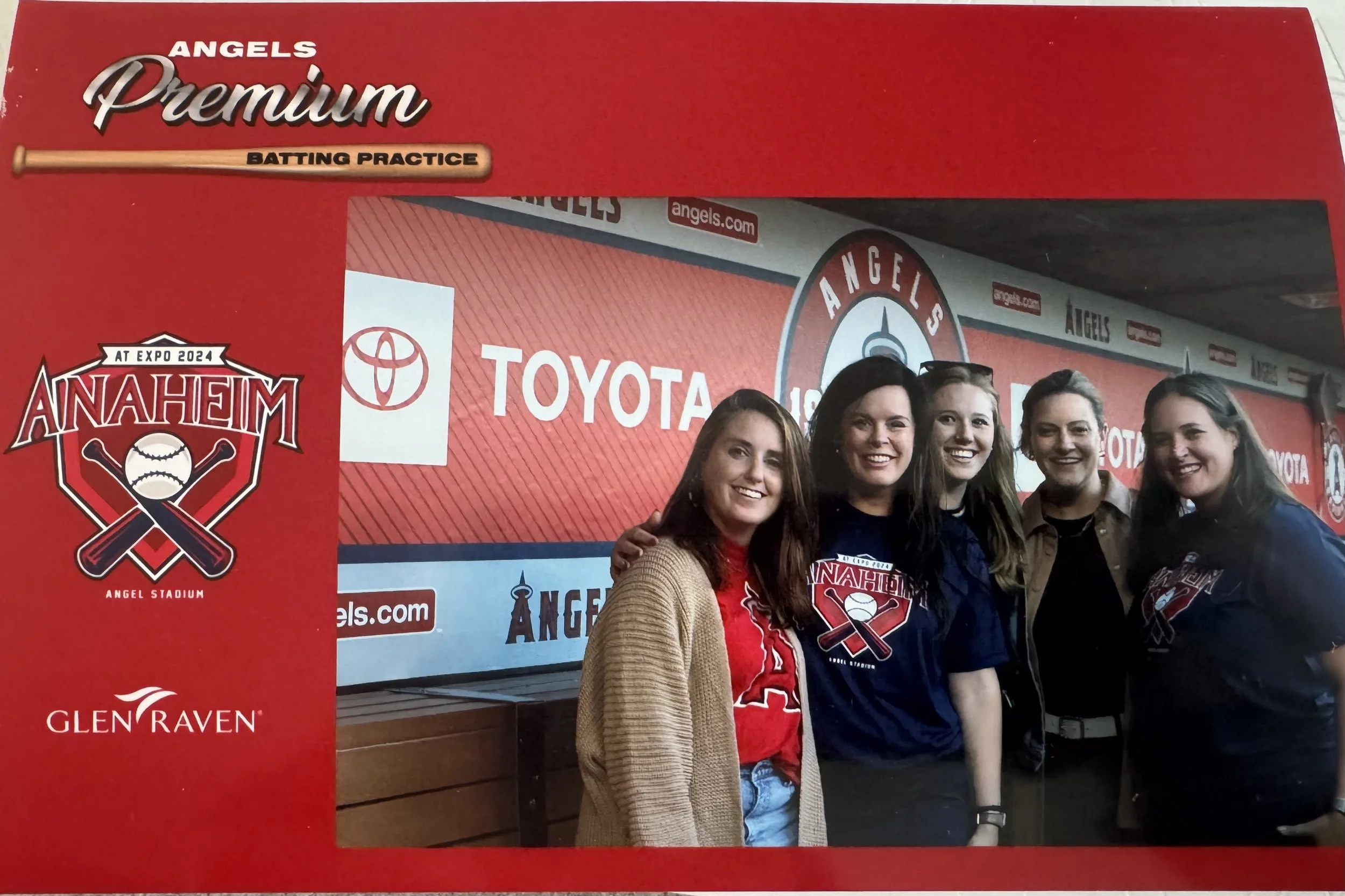 A group of women smiling and posing for a photo at Angels Baseball event inside Angel Stadium, with logos of Angels, Toyota, and Glen Raven visible on the background wall and a red promotional banner.