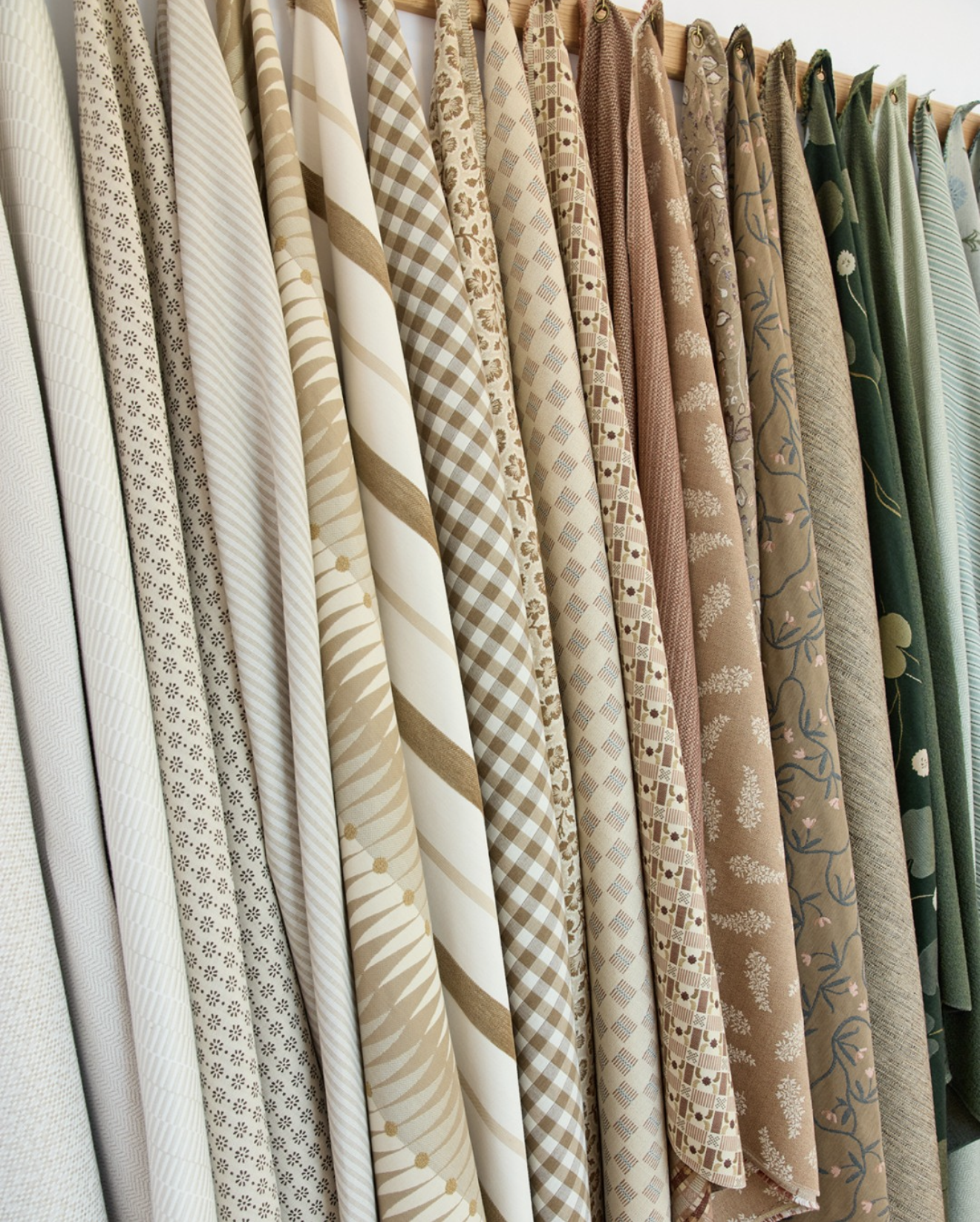 A row of fabric bolts with various beige, brown, and green patterned textiles hanging on a rack.