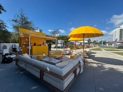 Outdoor lounge area with yellow umbrellas, white sofas, and a yellow bar or food stand under a clear blue sky.