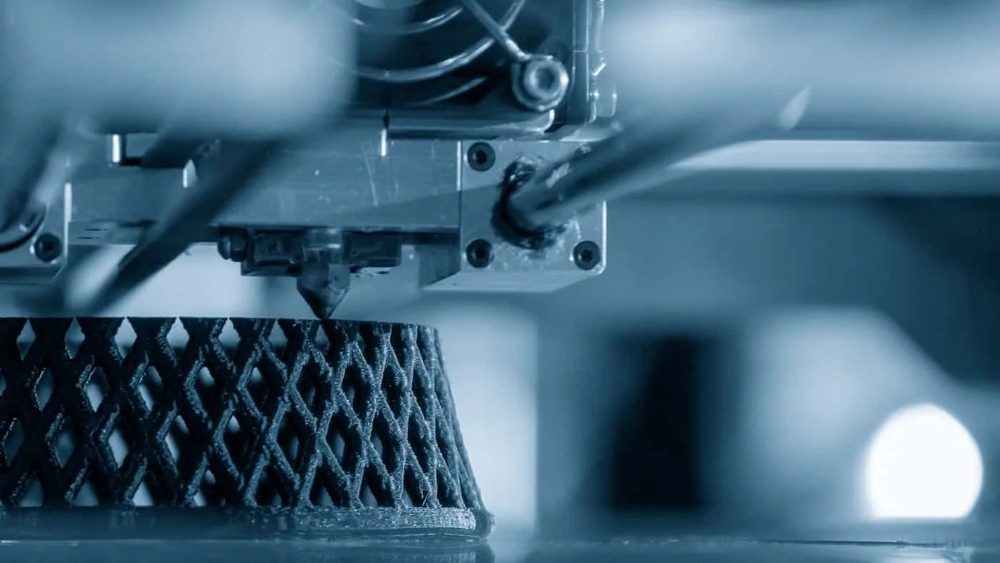 Close-up view of a 3D printer nozzle extruding filament onto a circular print bed.