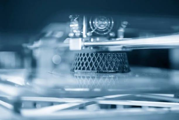 Close-up of a 3D printer with a black lattice-like object being printed.