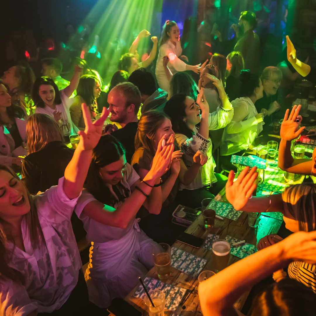People dancing and enjoying themselves at a lively party with colorful lights and drinks on the table.