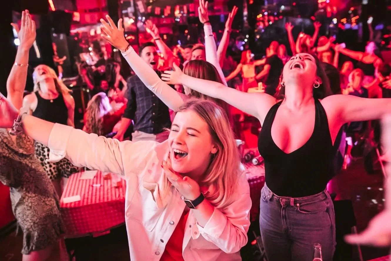 People dancing and celebrating in a lively party with red lighting, smiling and having fun.