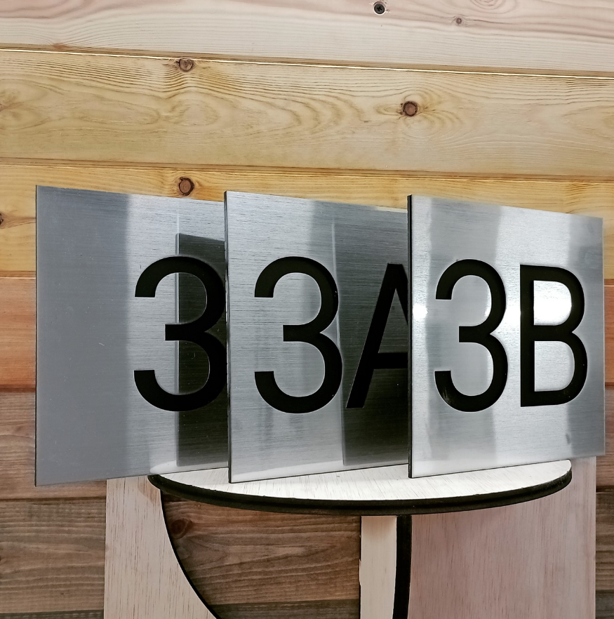 A modern metal address sign with the numbers 3343B displayed on three panels, mounted on a wooden wall.