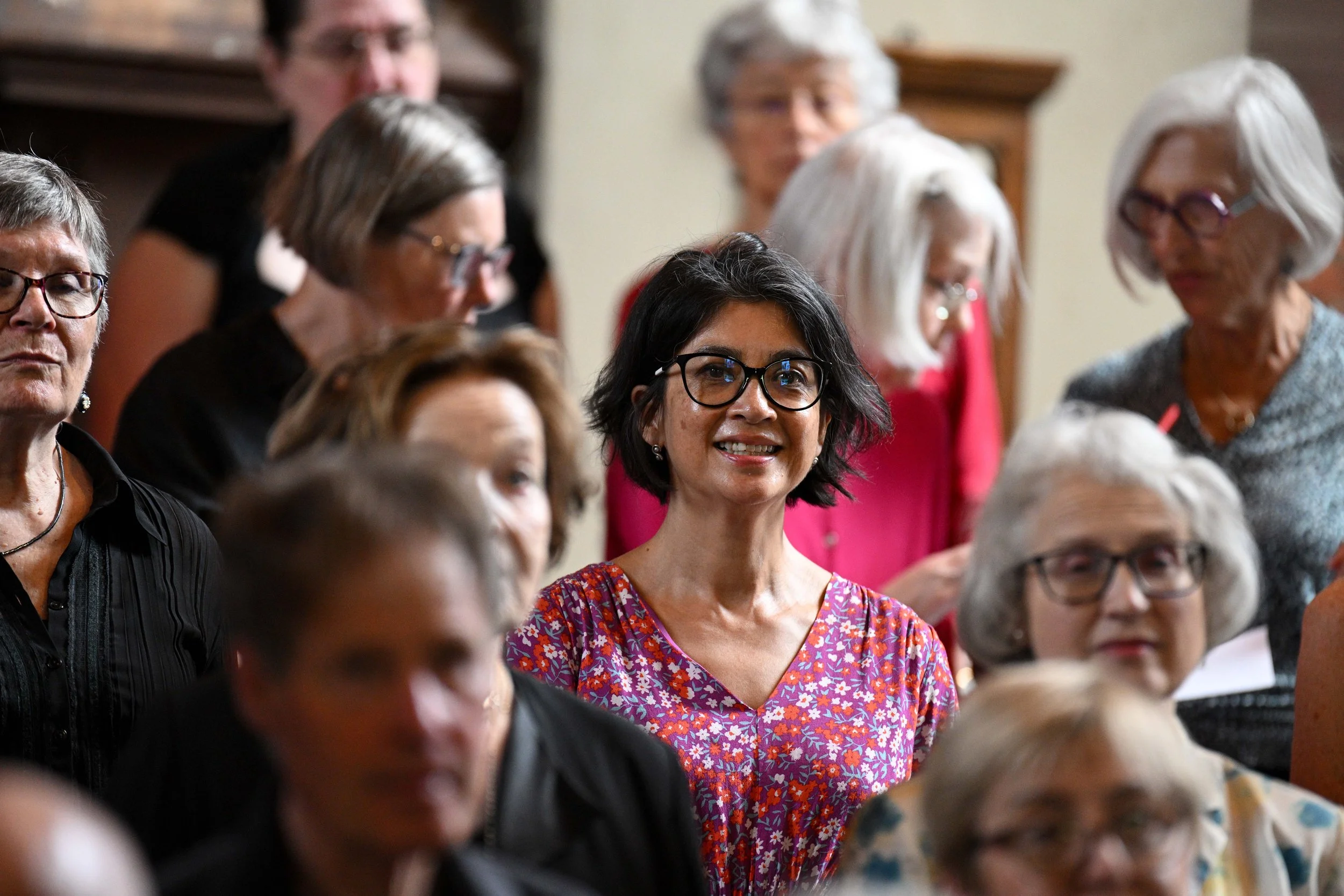 Group of women at a social gathering, with one woman with dark hair and glasses smiling in the center