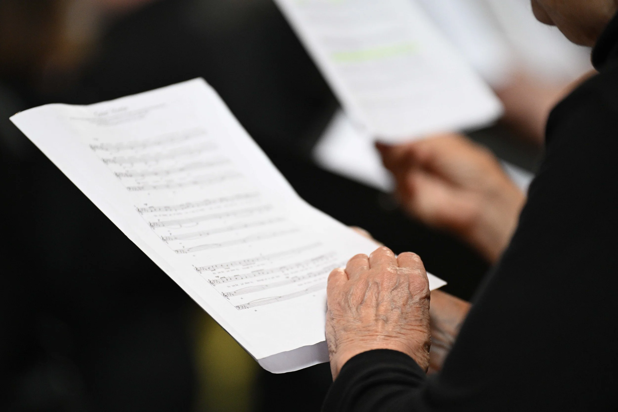 People holding and reading hymn or sheet music pages during a gathering or service.