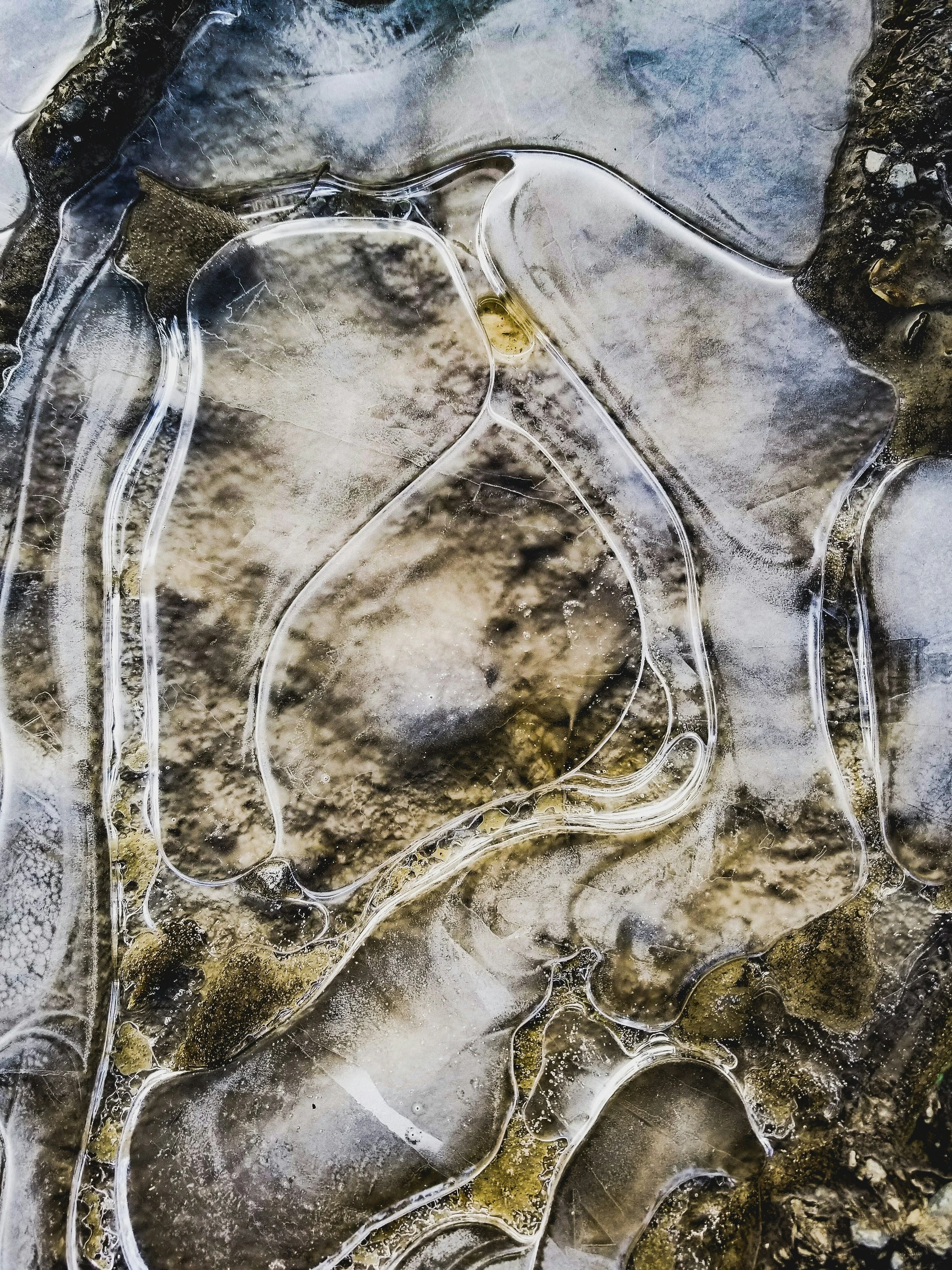 Close-up of ice with embedded dirt and debris, showing cracks and trapped air bubbles.