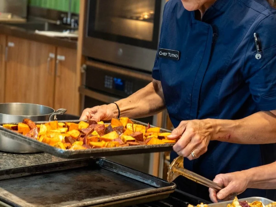 Chef placing roasted sweet potatoes on a baking sheet in a kitchen.