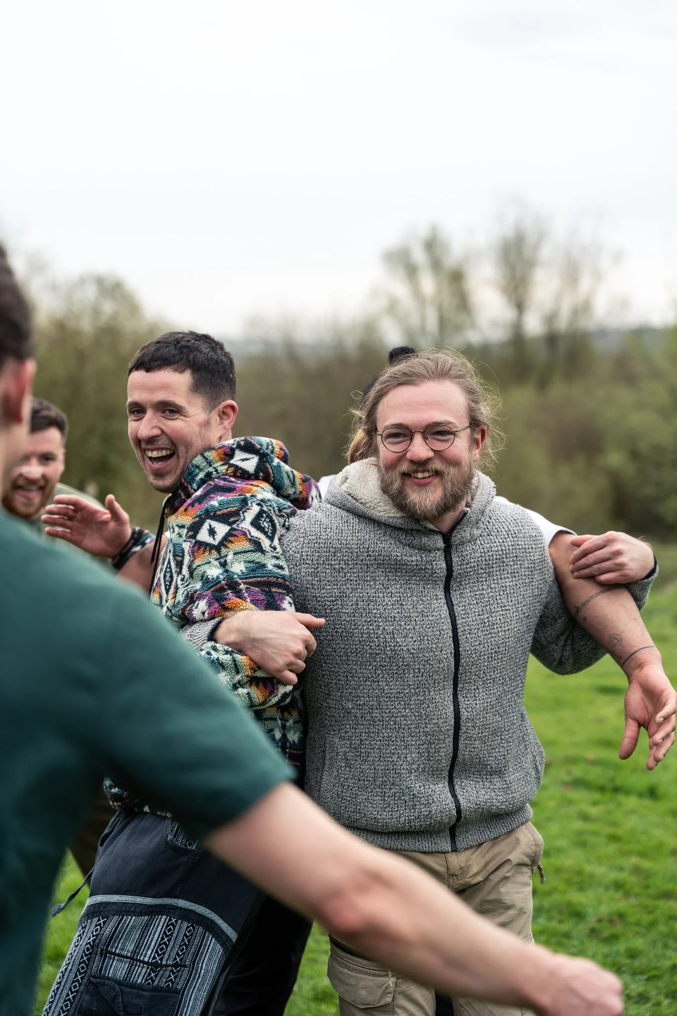 Group of people outdoors with arms around each other, smiling, on a cloudy day.