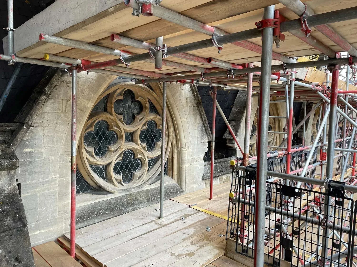 Scaffolding around a stone building with a large decorative stained glass window under restoration.