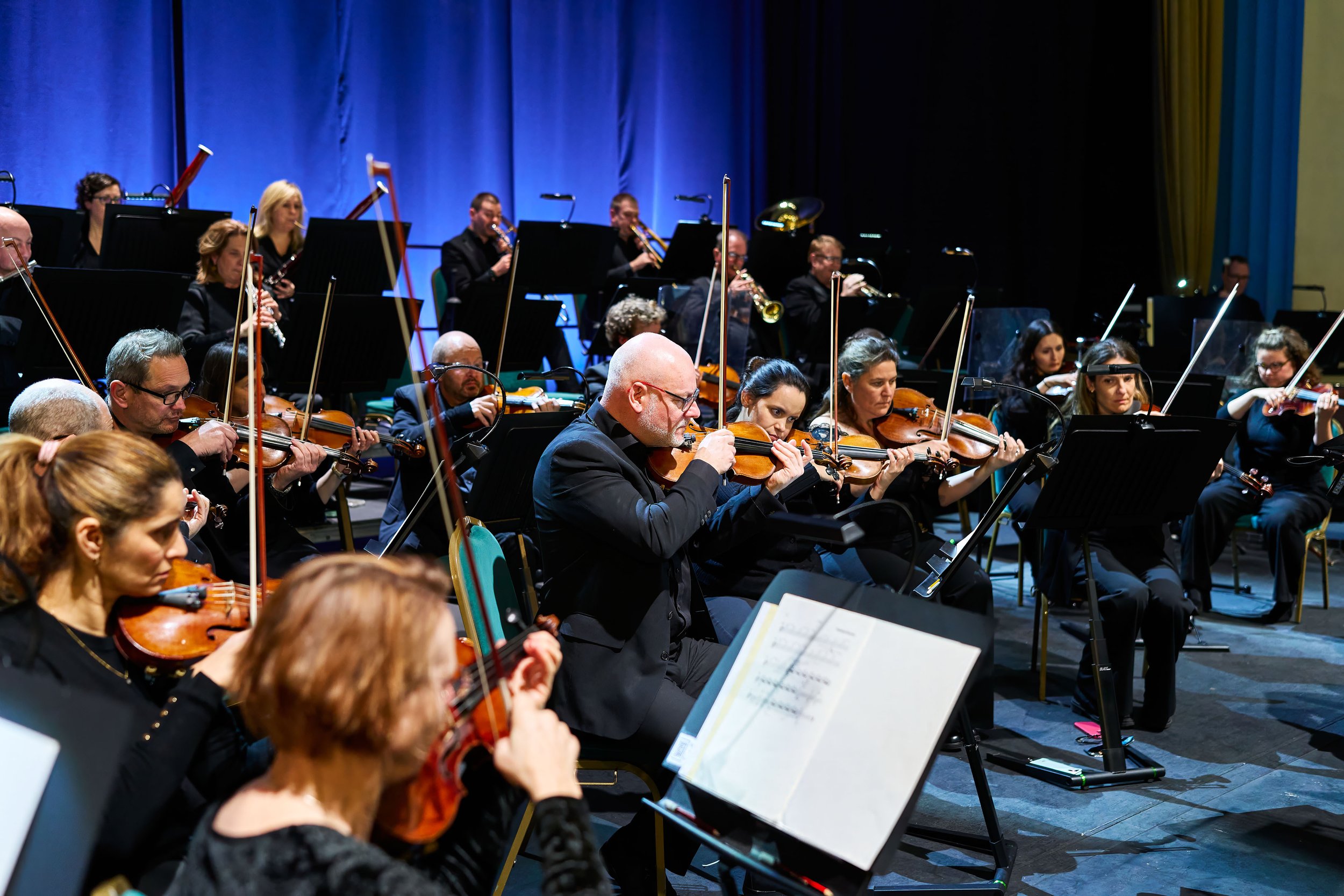 An orchestra performing on stage with musicians playing string and brass instruments.