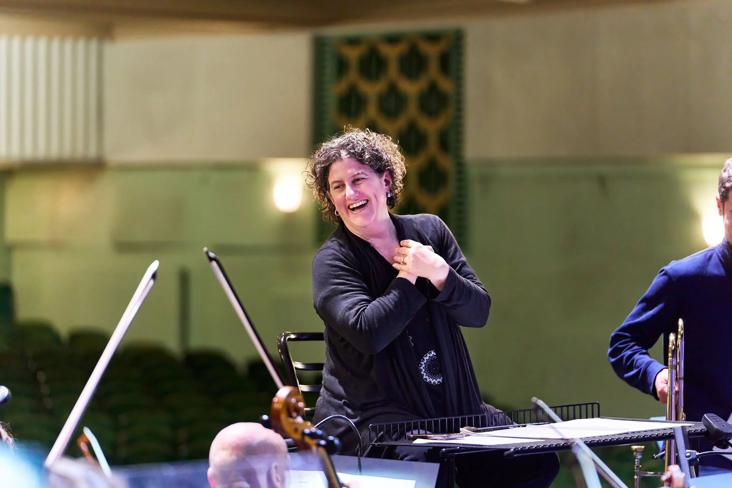 Conductor Rebecca Miller smiling during rehearsal with Bath Philharmonic Orchestra.