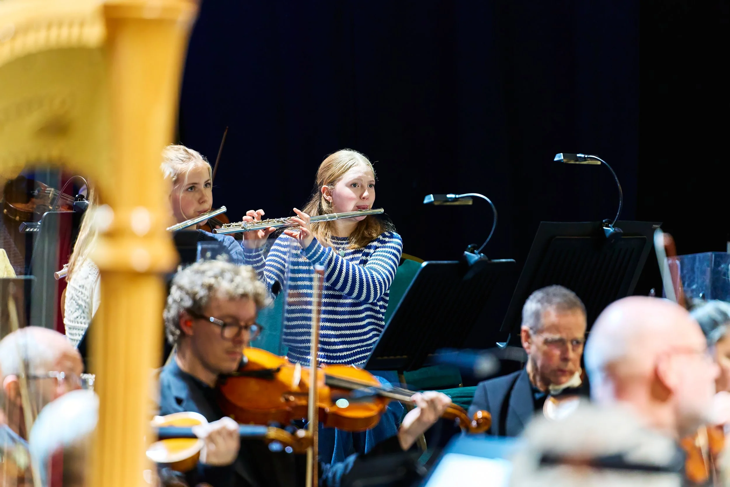 Young people play flute on stage with Bath Philharmonic Orchestra.
