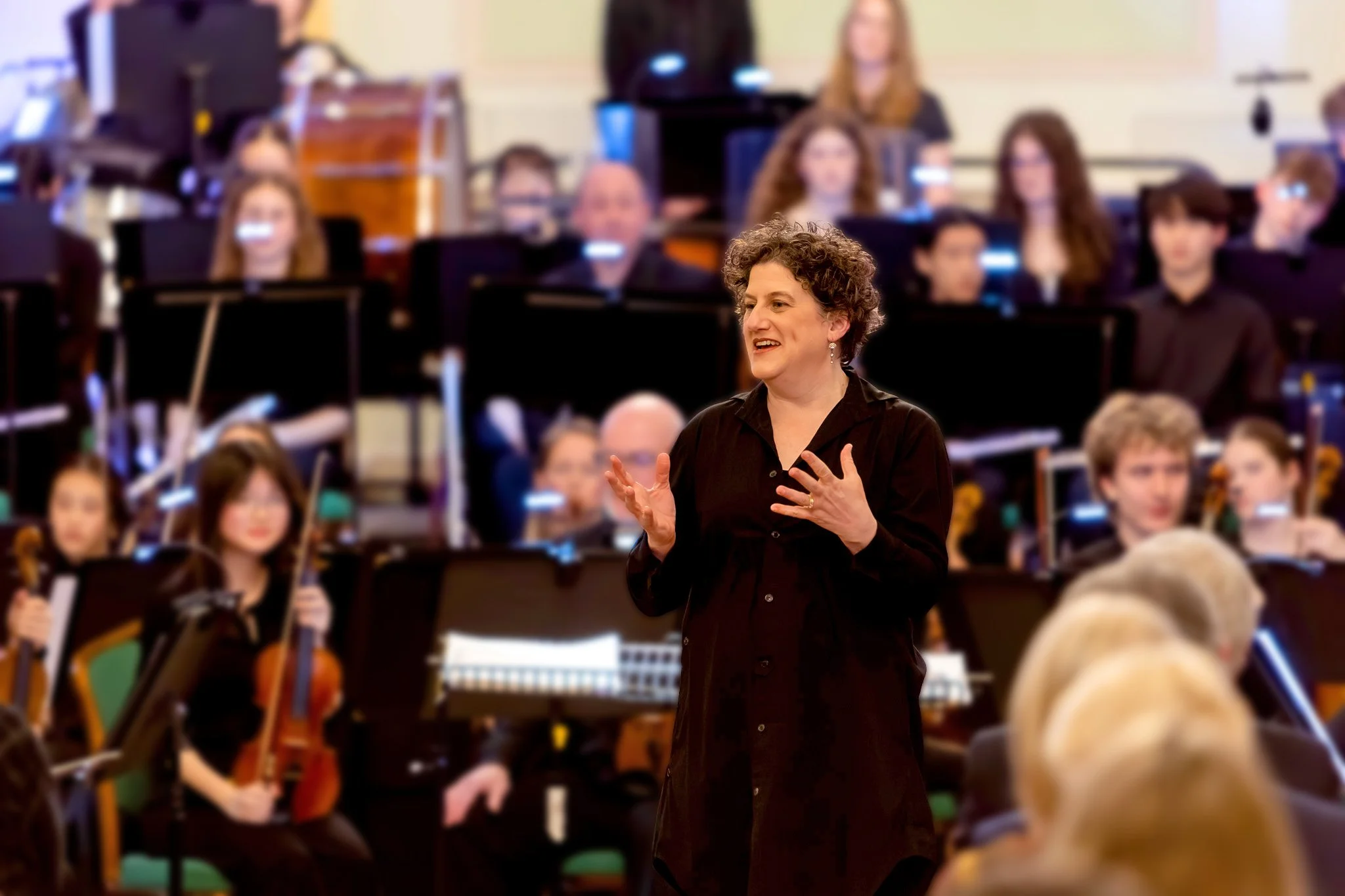 Conductor Rebecca Miller with Bath Philharmonic Orchestra and King Edward's School Senior Orchestra talking to the audience.
