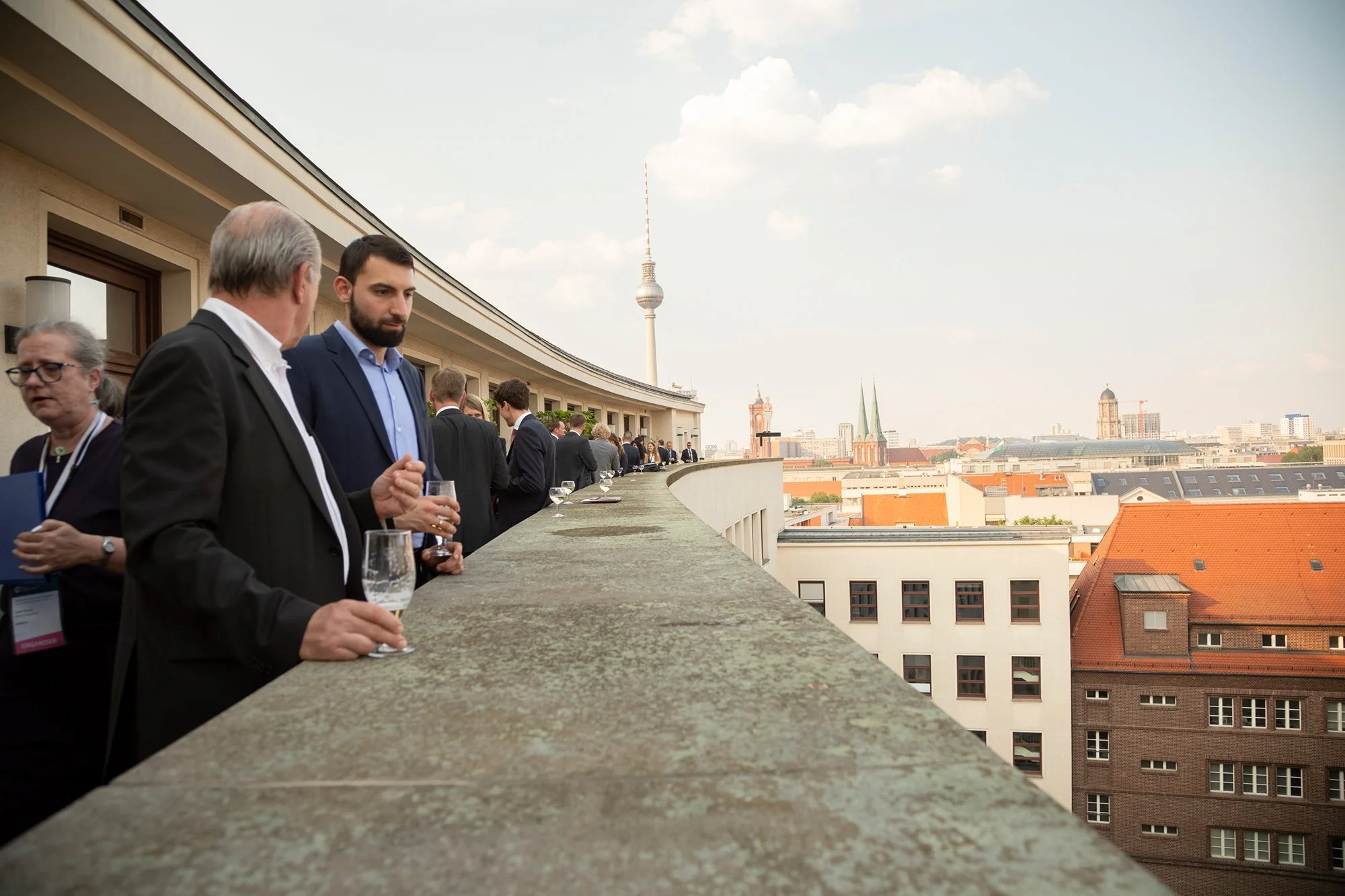 Menschen beim Networking auf einer Dachterrasse mit Blick auf die Berliner Fernsehkuppel und die Stadt.