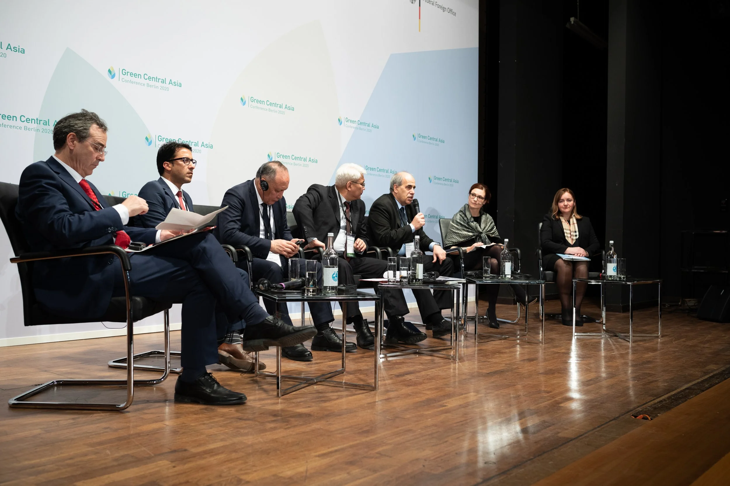 Fünf Personen sitzen auf einer Bühne bei einer Konferenz, die im Rahmen eines internationalen Forums stattfindet, mit einem großen Bildschirm im Hintergrund, auf dem 'Green Central Asia' und 'Conference Berlin 2020' zu sehen sind.