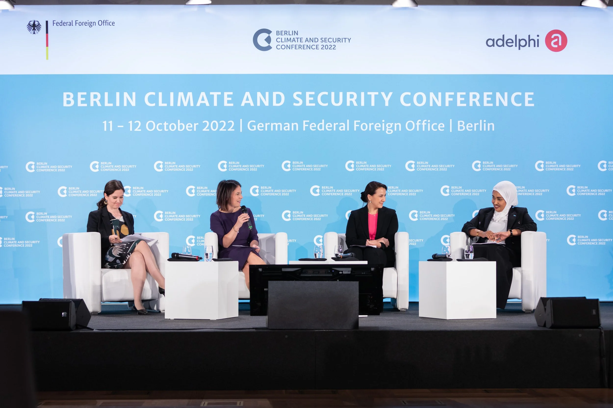 Vier Frauen sitzen auf einer Bühne bei der Berlin Climate and Security Conference 2022, die vom Bundesauswärtigen Amt organisiert wird. Im Hintergrund ist ein Banner mit den VeranstaltungDetails und Logos zu sehen.